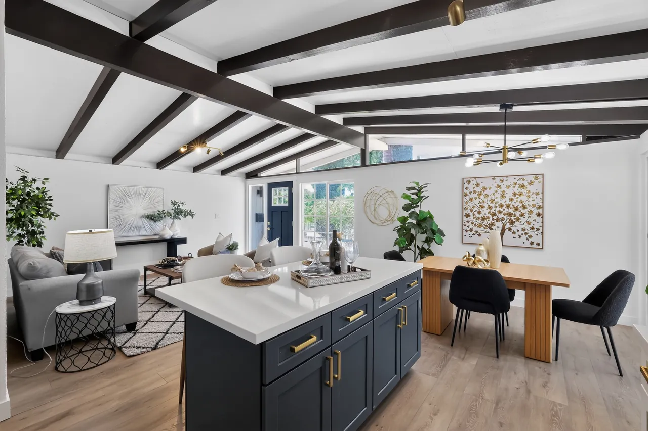 Renovated open-concept kitchen with a navy island, exposed ceiling beams and staged dining area prepared for listing photos