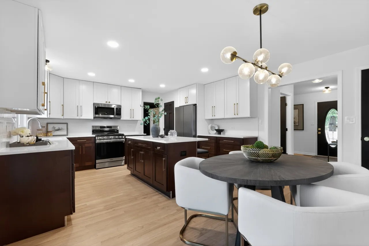 Updated kitchen with white upper cabinets, dark lower cabinets, a center island and a round dining table