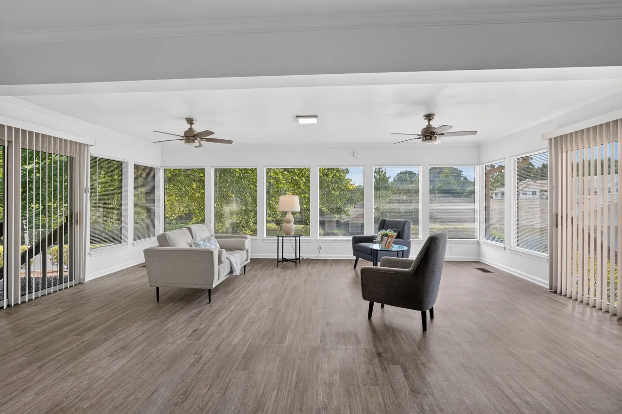 Bright sunroom with walls of windows, ceiling fans and simple staged seating