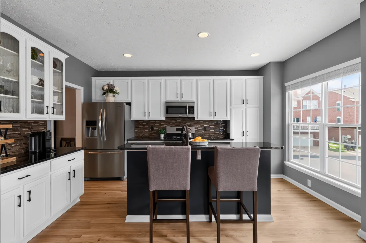 Kitchen with white cabinets, glass-front uppers, a dark island with bar stools and stainless appliances