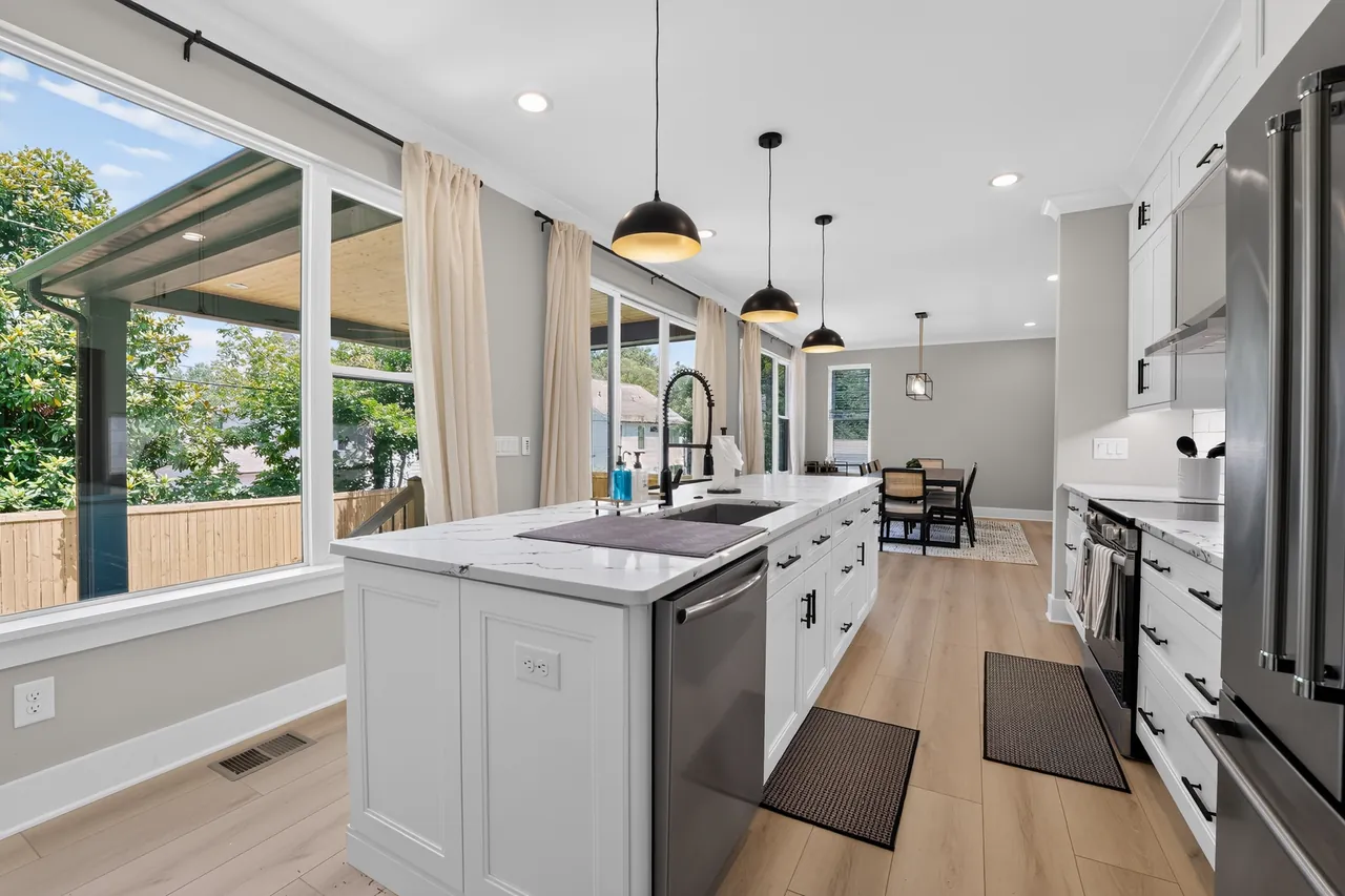 Bright kitchen with white shaker cabinets, a marble-look island, black pendant lights and light wood floors