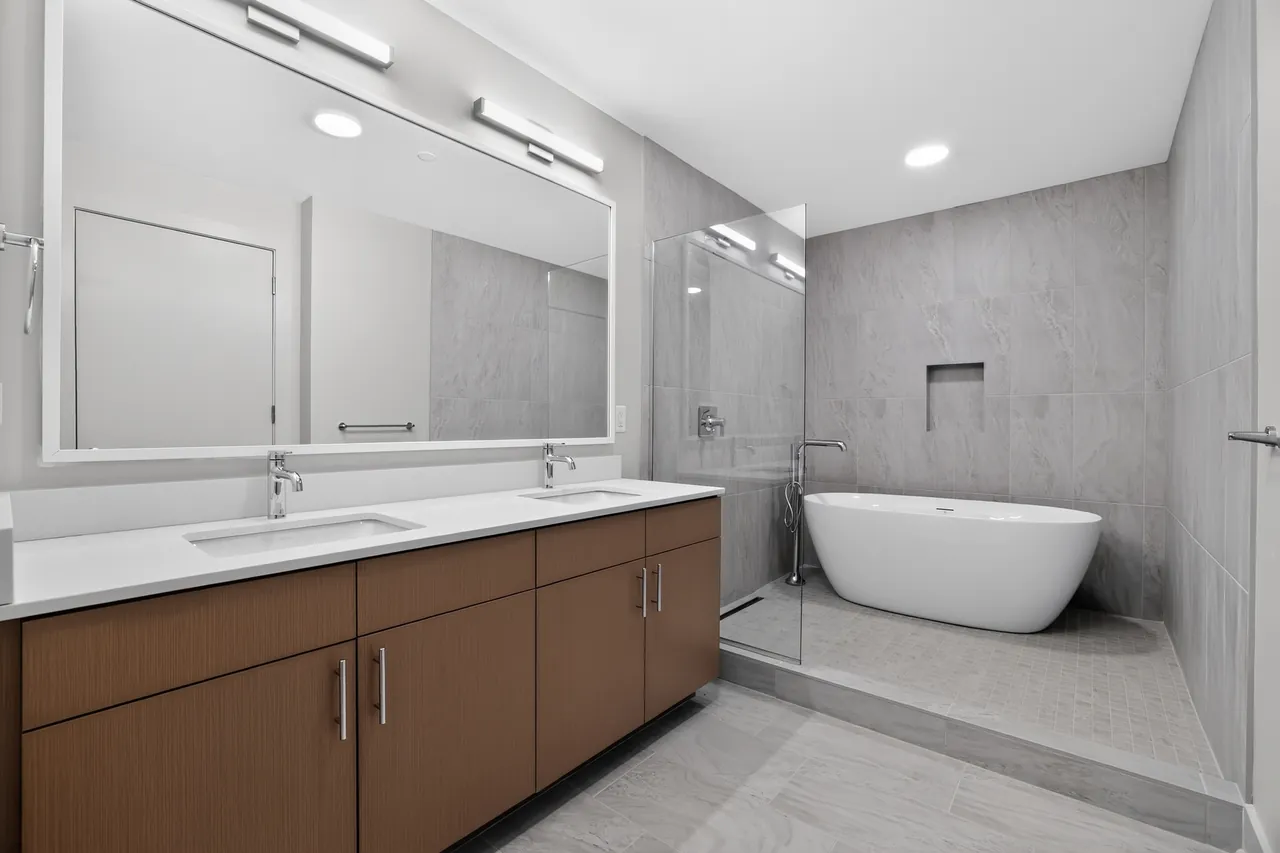 Updated bathroom with a double vanity, large mirror, freestanding tub and glass-enclosed tile shower